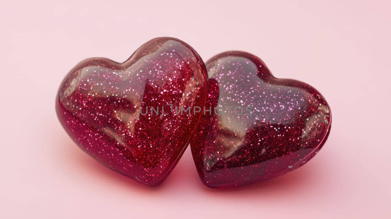 Two red glass hearts with glitters on pink background. St. Valentine's day concept. Symbol of love, romance and passion.