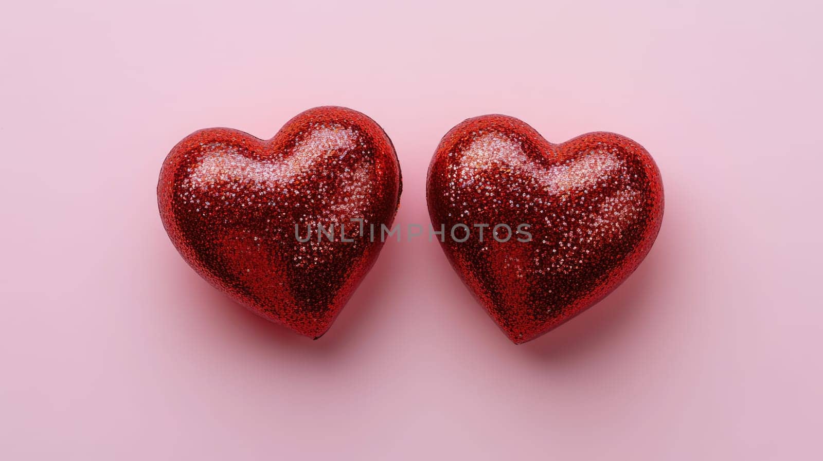 Two red glass hearts with glitters on pink background. St. Valentine's day concept. Symbol of love, romance and passion.