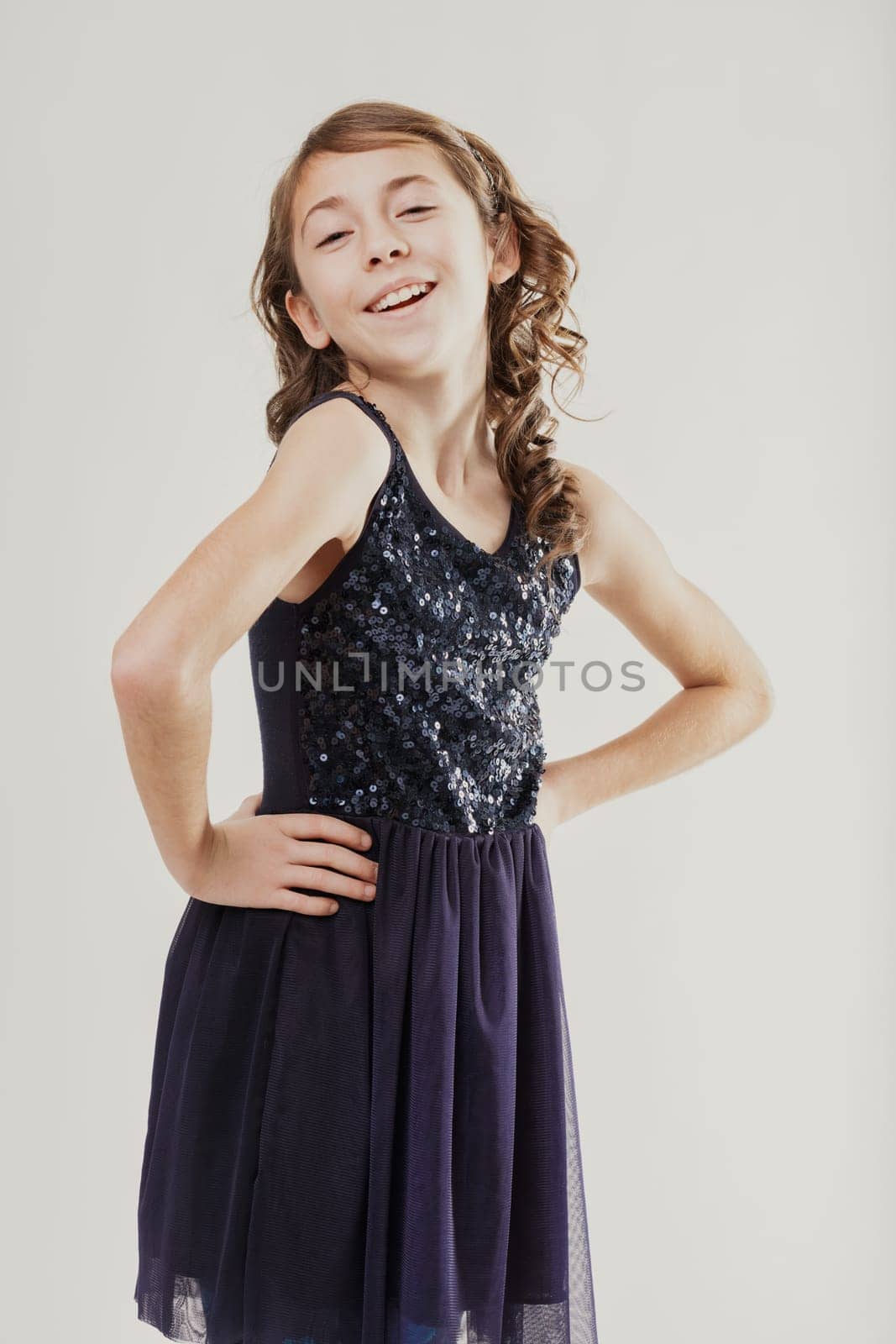 Cheerful preteen girl wearing a sparkling sequined dress, posing confidently with hands on her hips and radiating joy through her bright smile in a studio setting