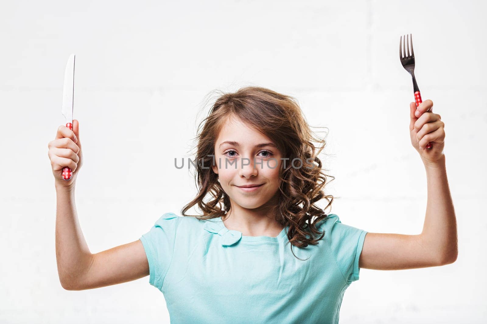 Elementary age girl confidently holding a fork and knife, expressing playful anticipation and joy for a meal, capturing youthful energy and eagerness