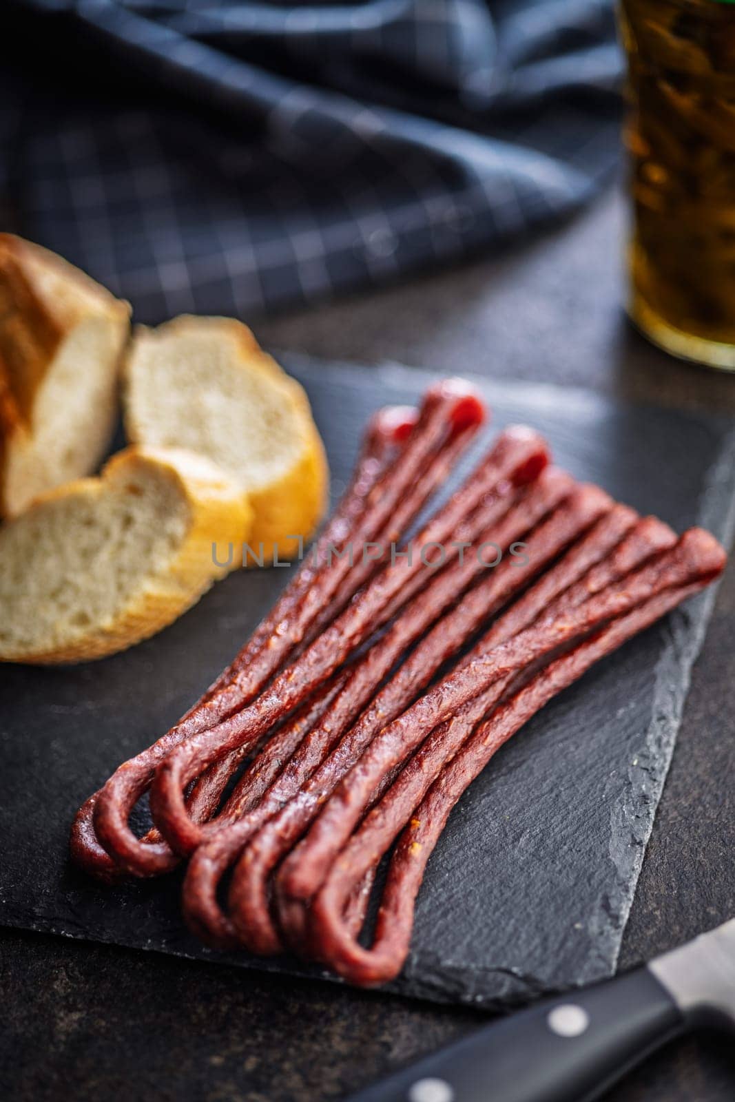 Smoked kabanos. Mini dried thin sausages on cutting board on a black table.