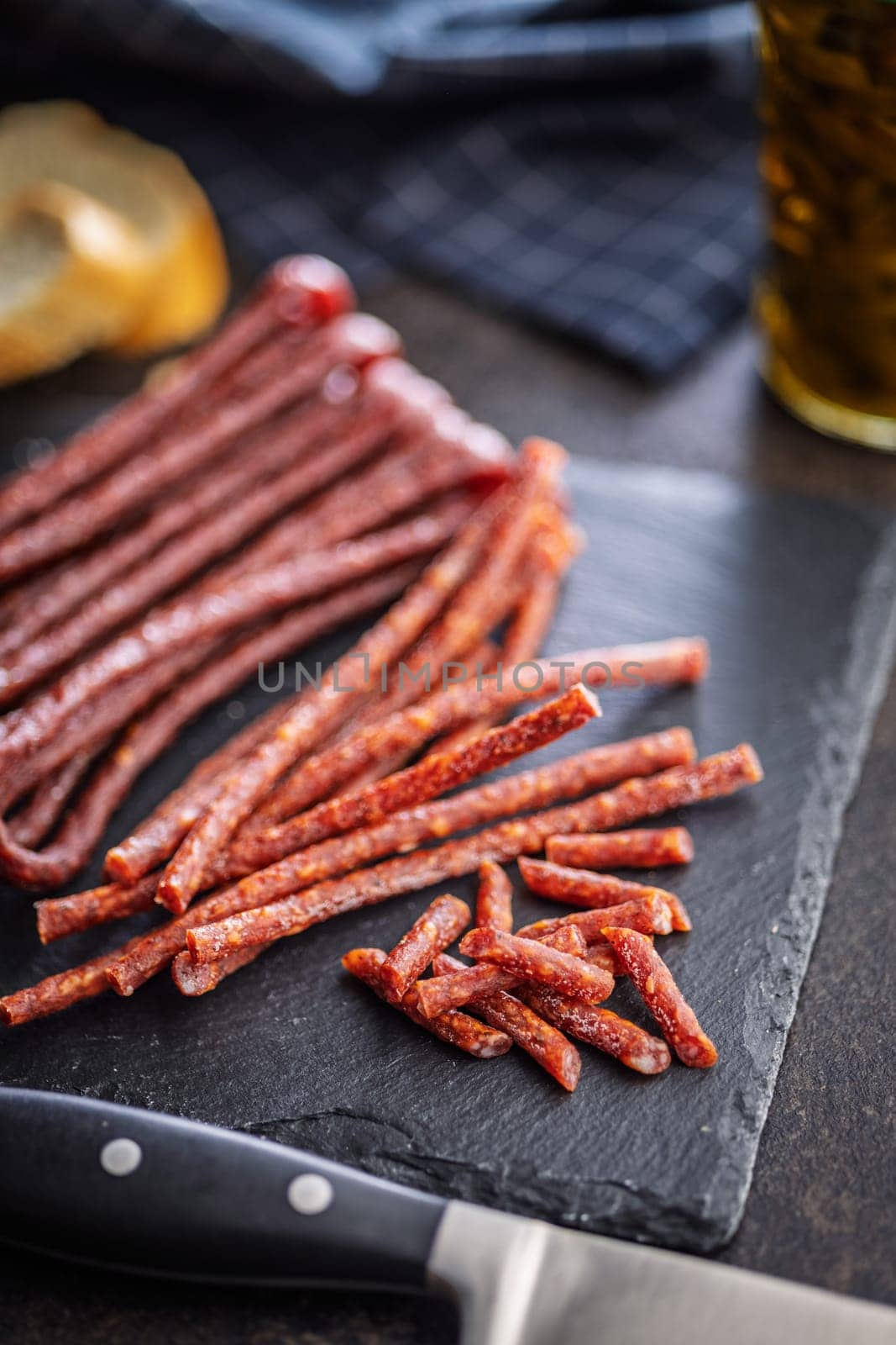 Smoked kabanos. Mini dried thin sausages on cutting board on a black table.