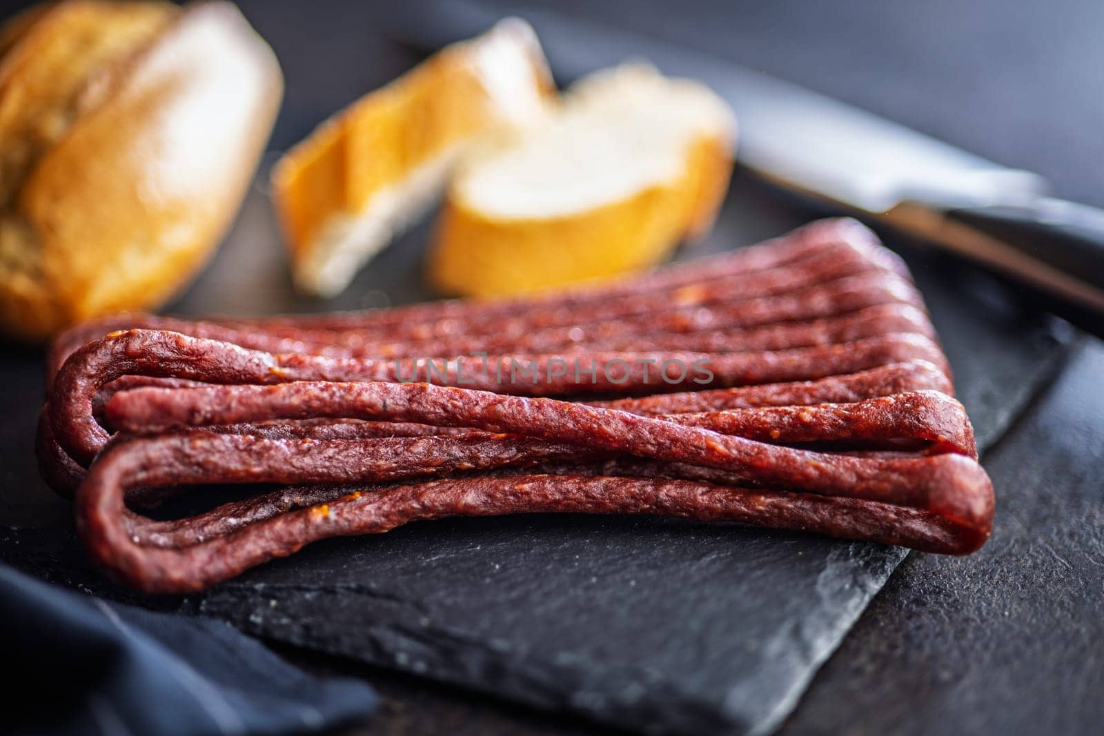 Smoked kabanos. Mini dried thin sausages on cutting board on a black table.