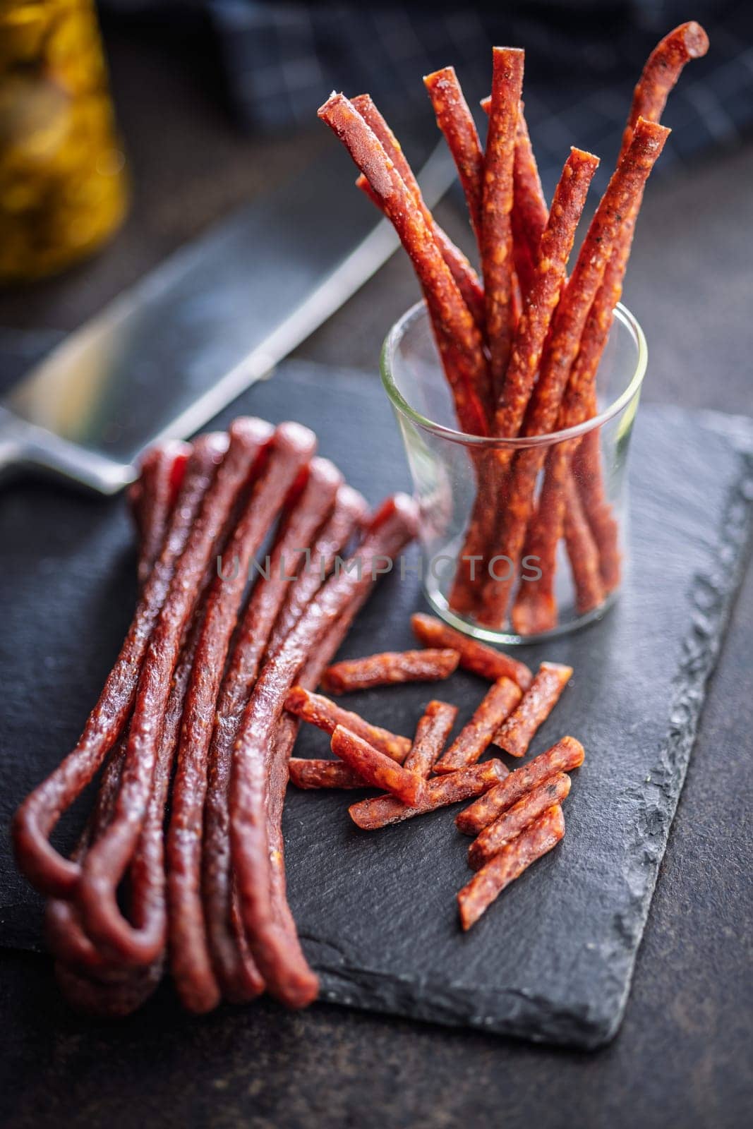 Smoked kabanos. Mini dried thin sausages on cutting board on a black table.