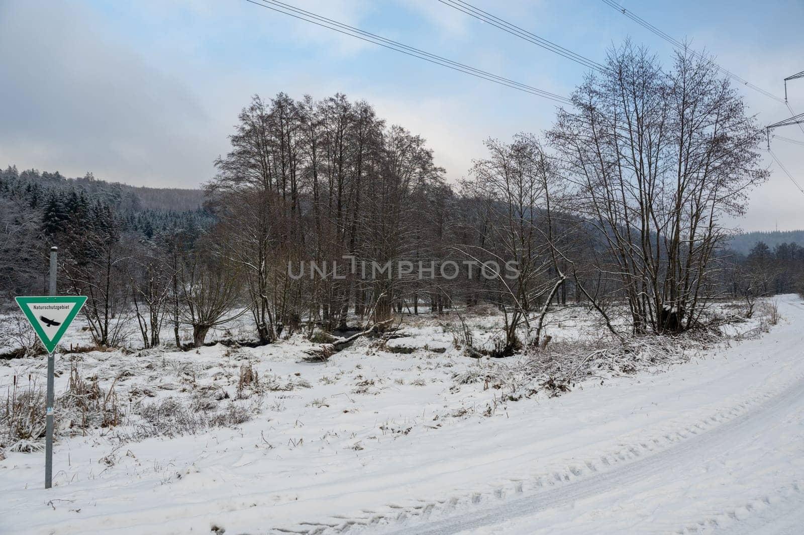 Winter landscape with lots of snow, trees, dirt road and a sign with the inscription "Nature reserve"" in German"