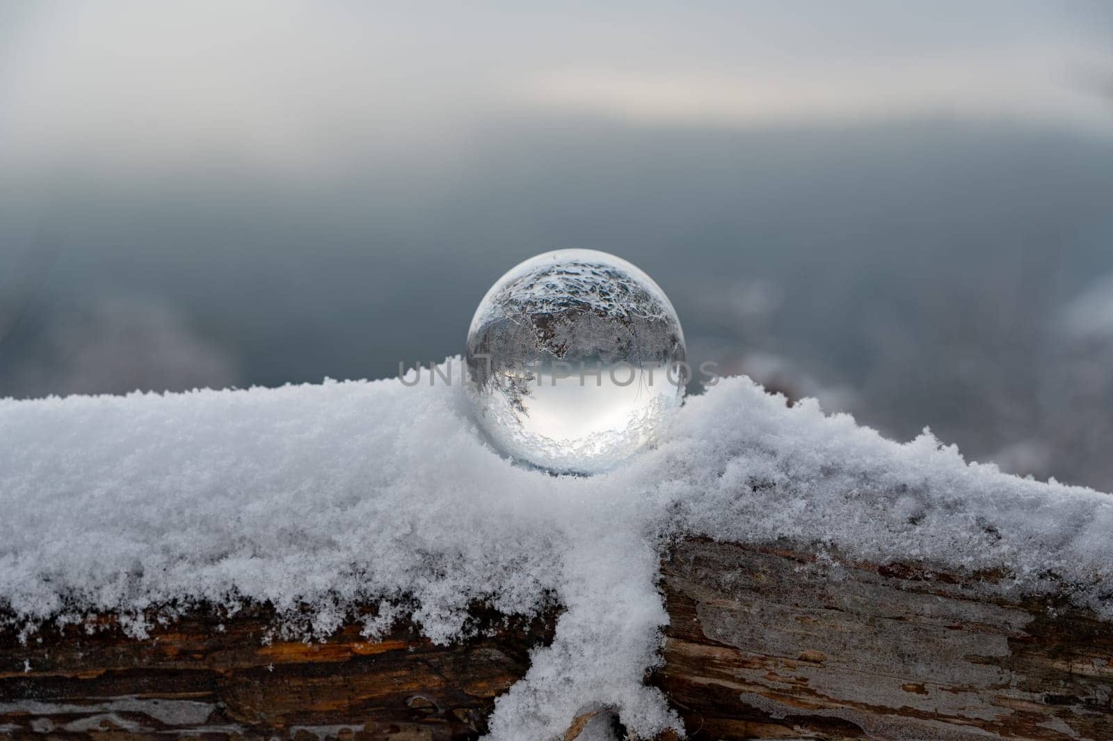 Glass ball on a wood on a cold winter day, with reflections of trees and snow in the glass