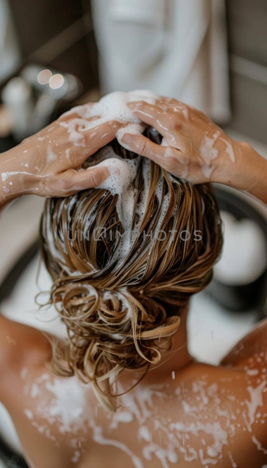 Close-up view of a person's hands gently massaging shampoo into wet, dark hair, creating a calming, therapeutic experience