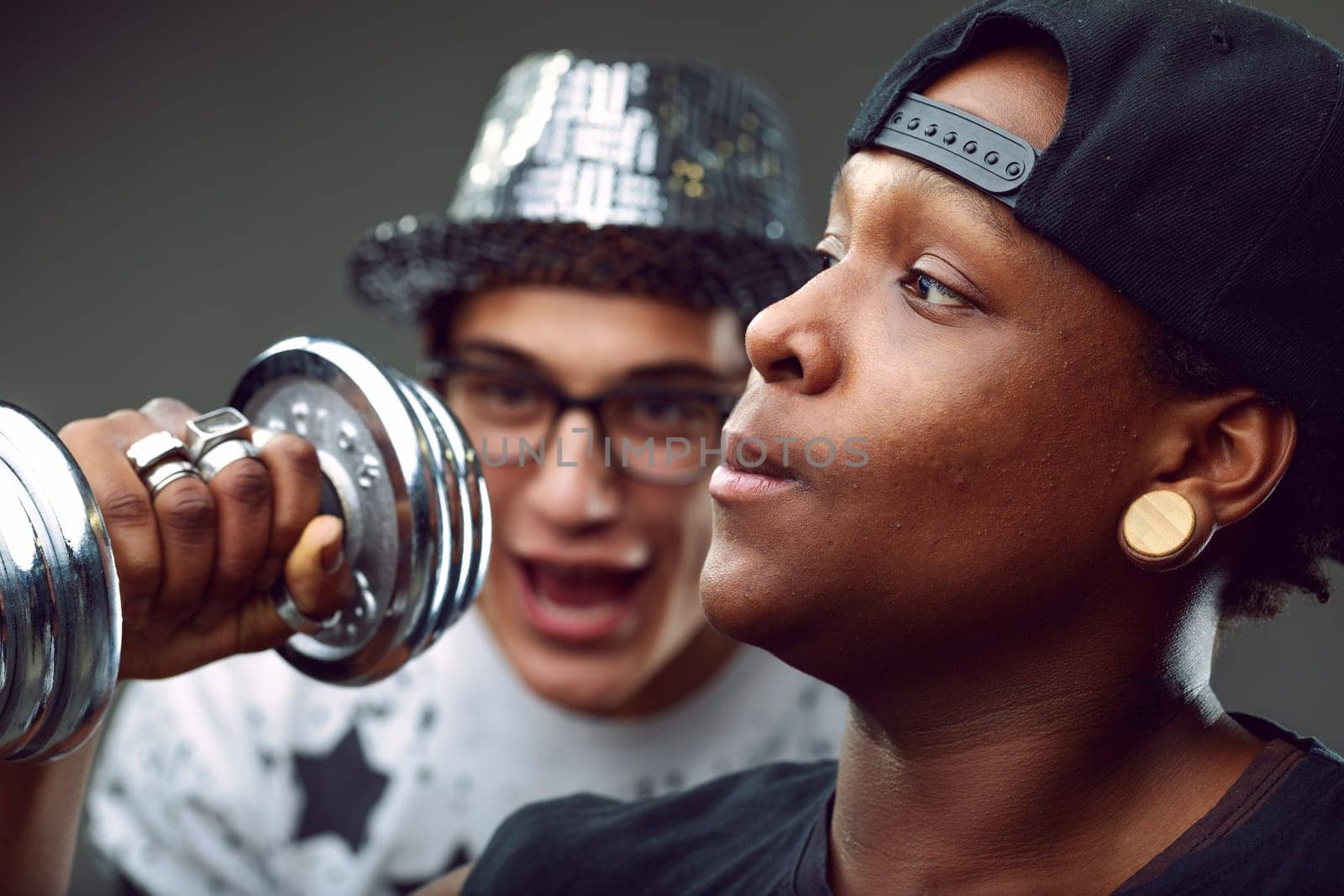 Two young men enjoying their workout together, one lifting a dumbbell while the other enthusiastically cheering him on, embodying friendship and motivation in their fitness journey