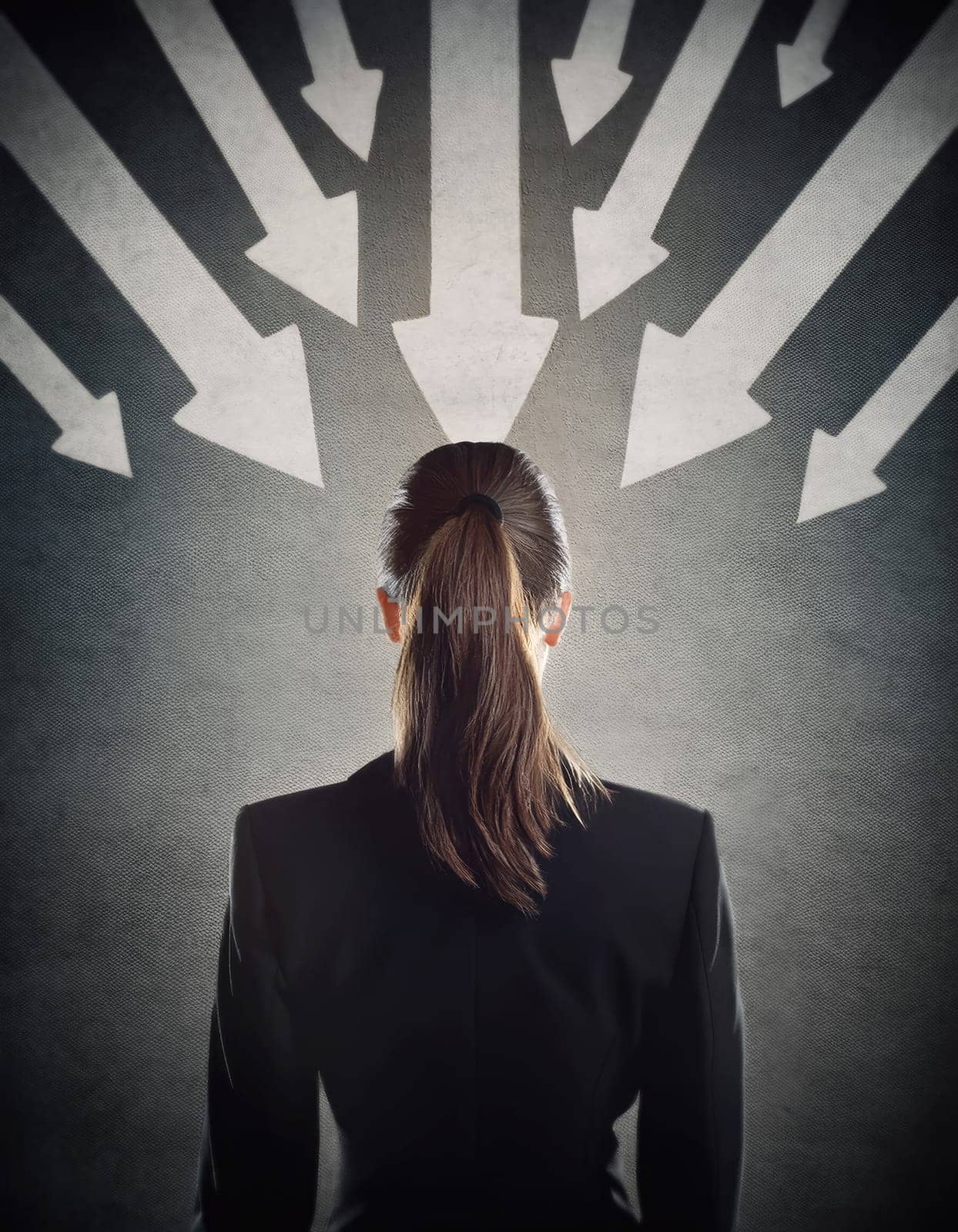 Rear view businesswoman in a dark room with multiple arrows pointing towards her, blaming as guilty person. Leading business under big pressure, social victim concept