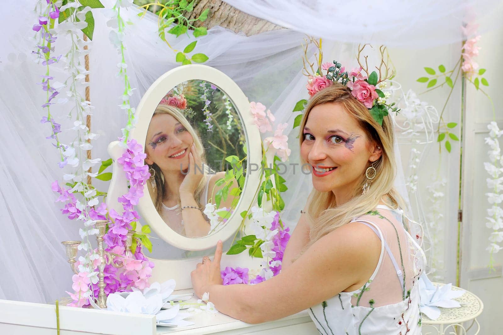 A pretty elf with flowers in her hair sits in front of an enchanted mirror