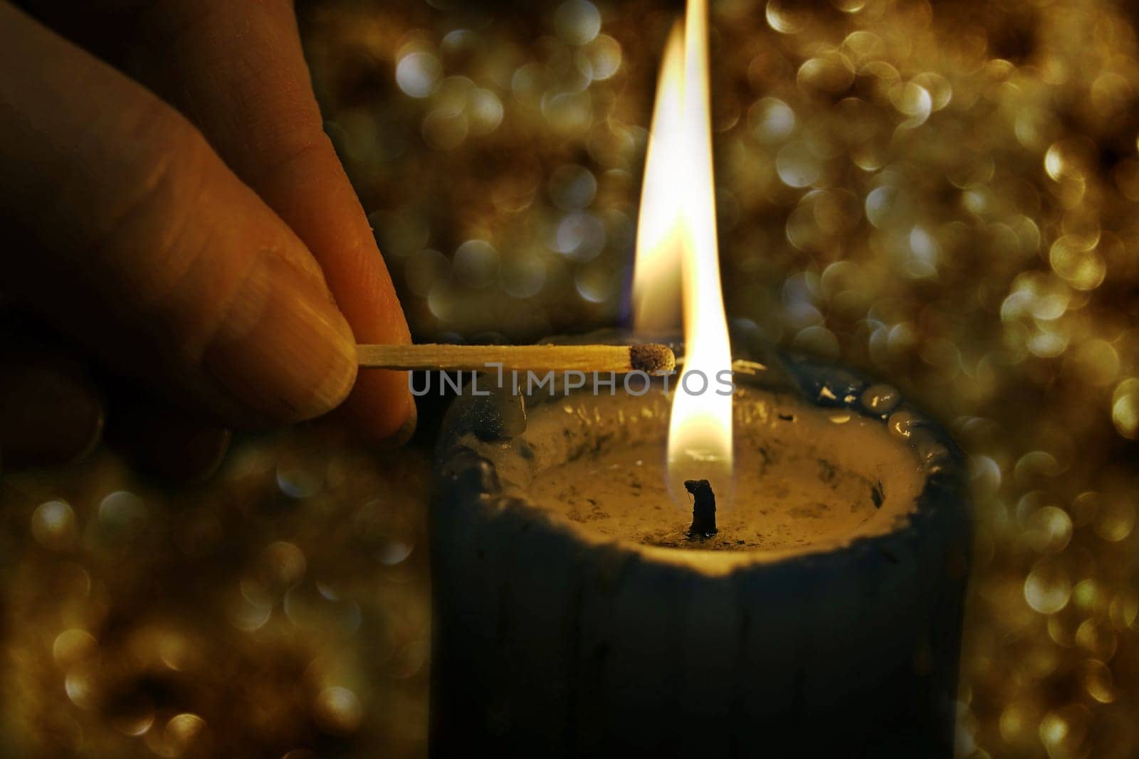 A woman lights a candle with a match in front of a glittering background