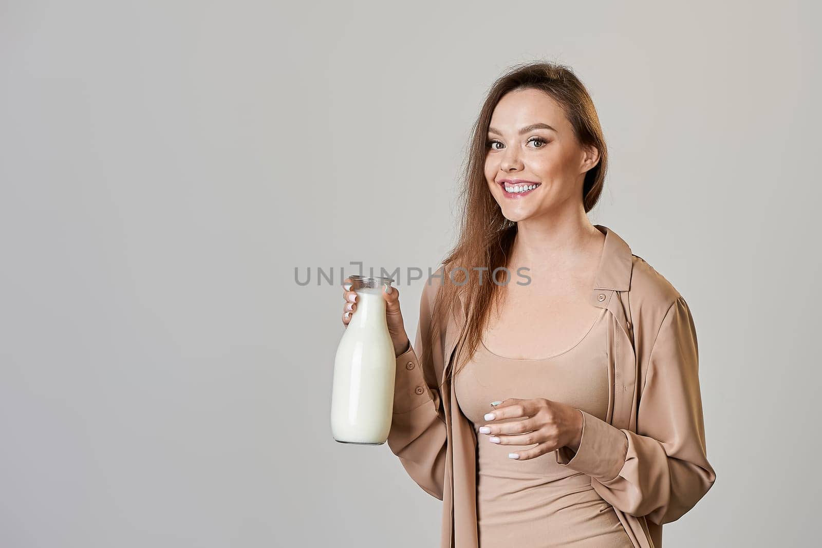 beautiful young woman drinking milk from a bottle on a gray background. High quality photo