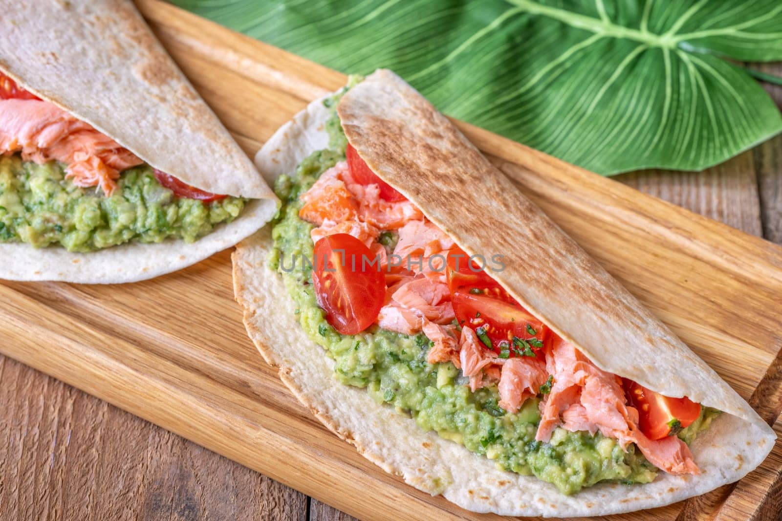 Two tacos filled with guacamole, baked salmon, and tomatoes on a rustic wooden table