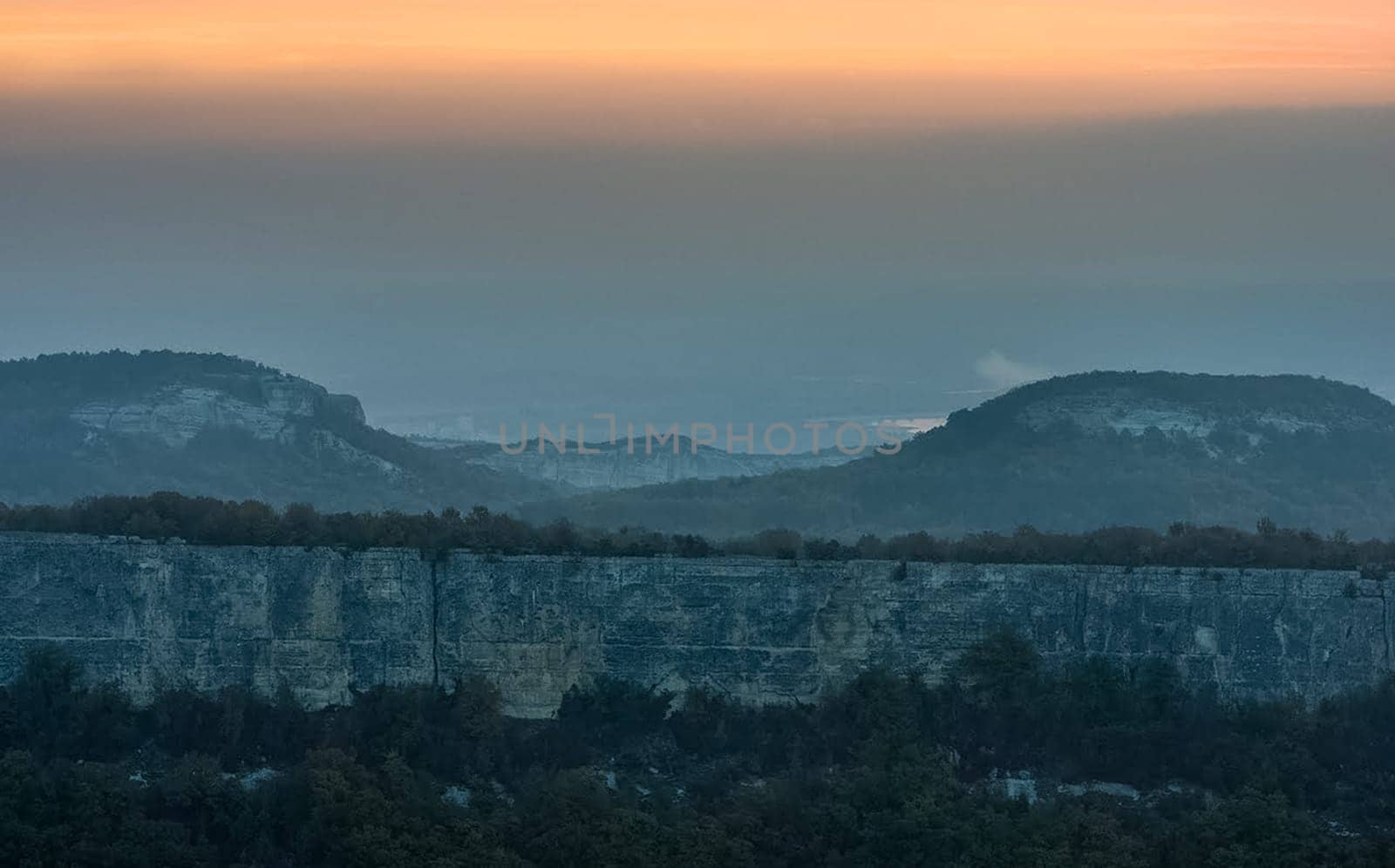 Dawn in the mountains of Crimea. A light haze of mist over the mountains and rays of the sun through the clouds.