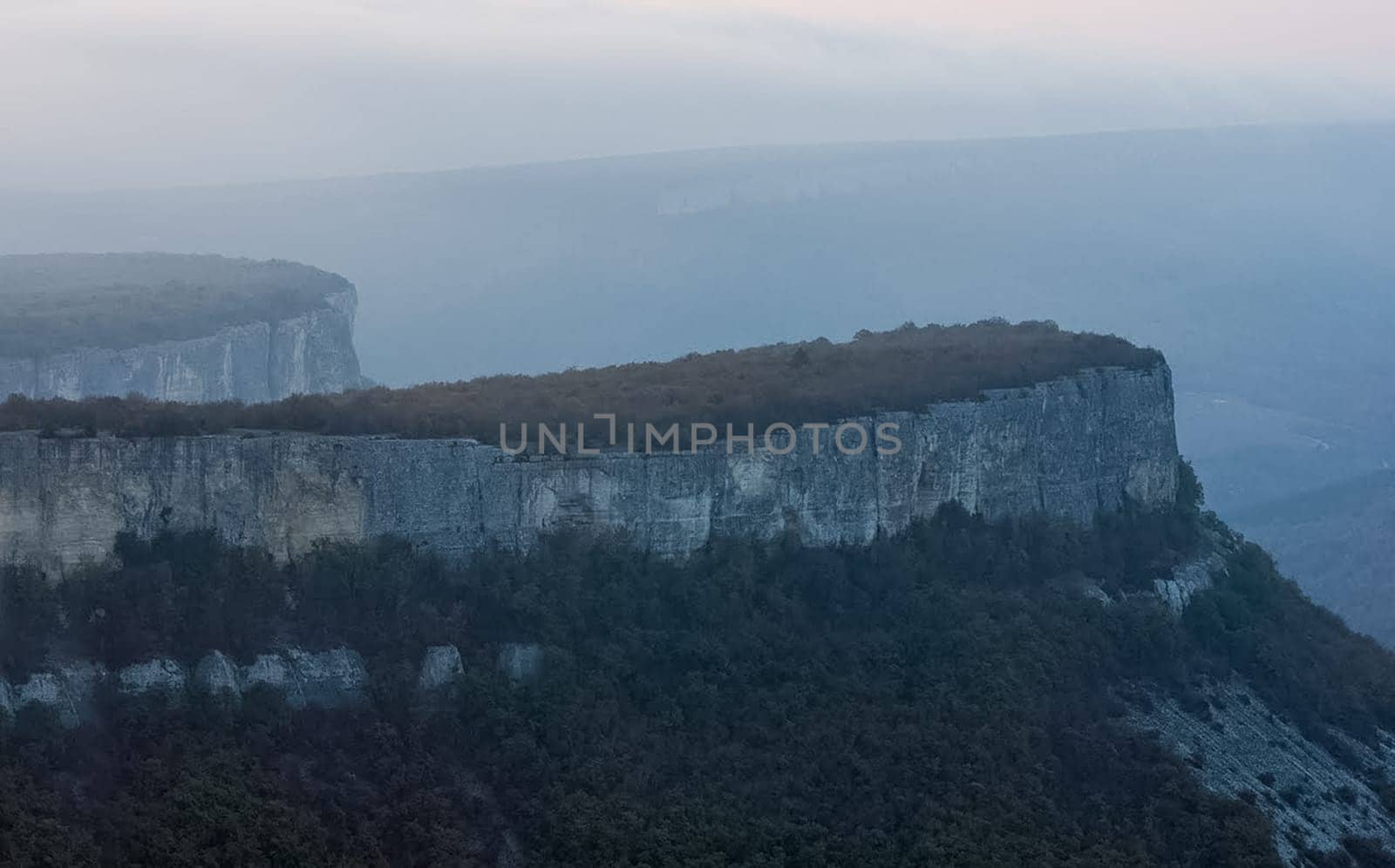 Dawn in the mountains of Crimea. A light haze of mist over the mountains and rays of the sun through the clouds.