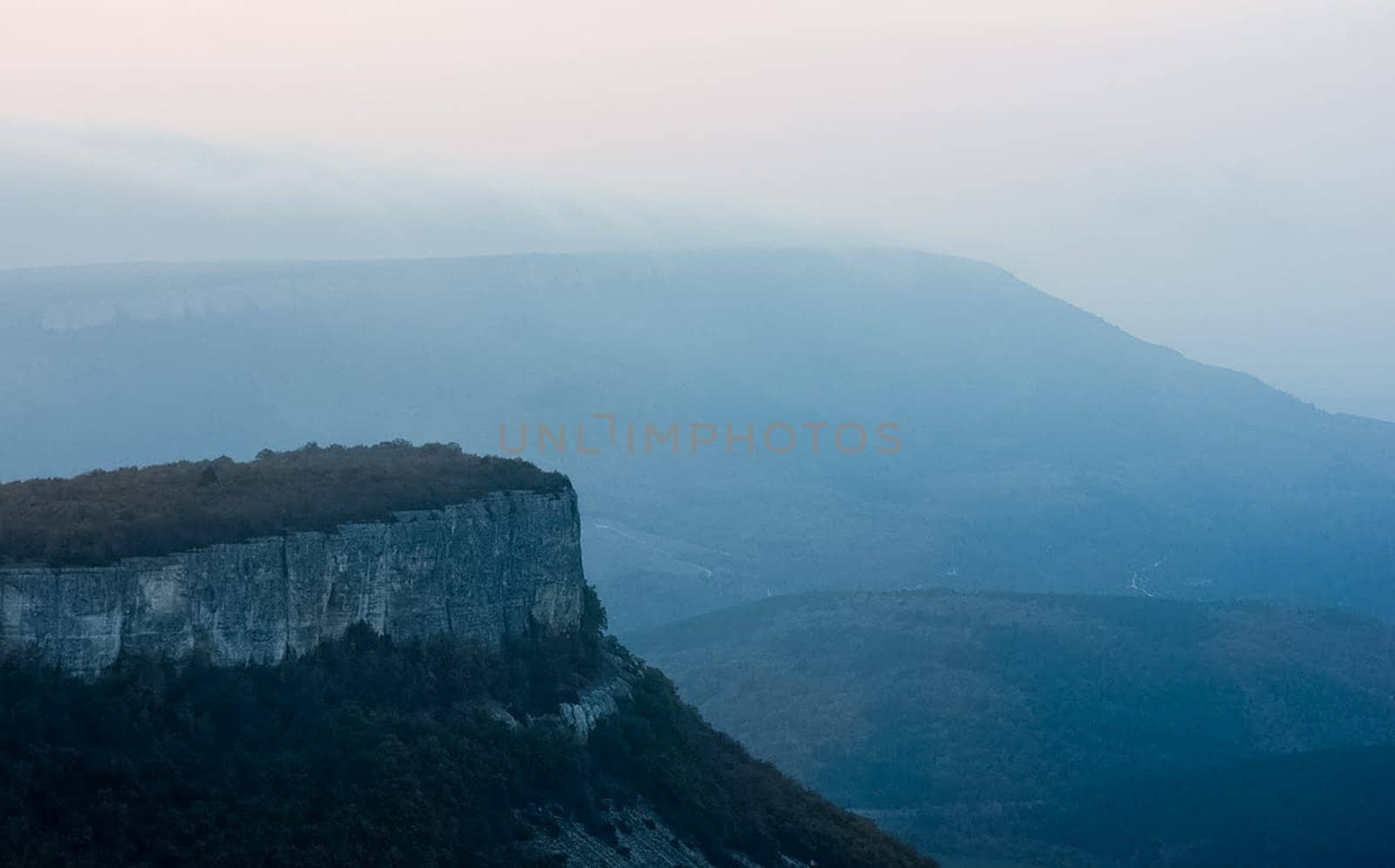 Dawn in the mountains of Crimea. A light haze of mist over the mountains and rays of the sun through the clouds.