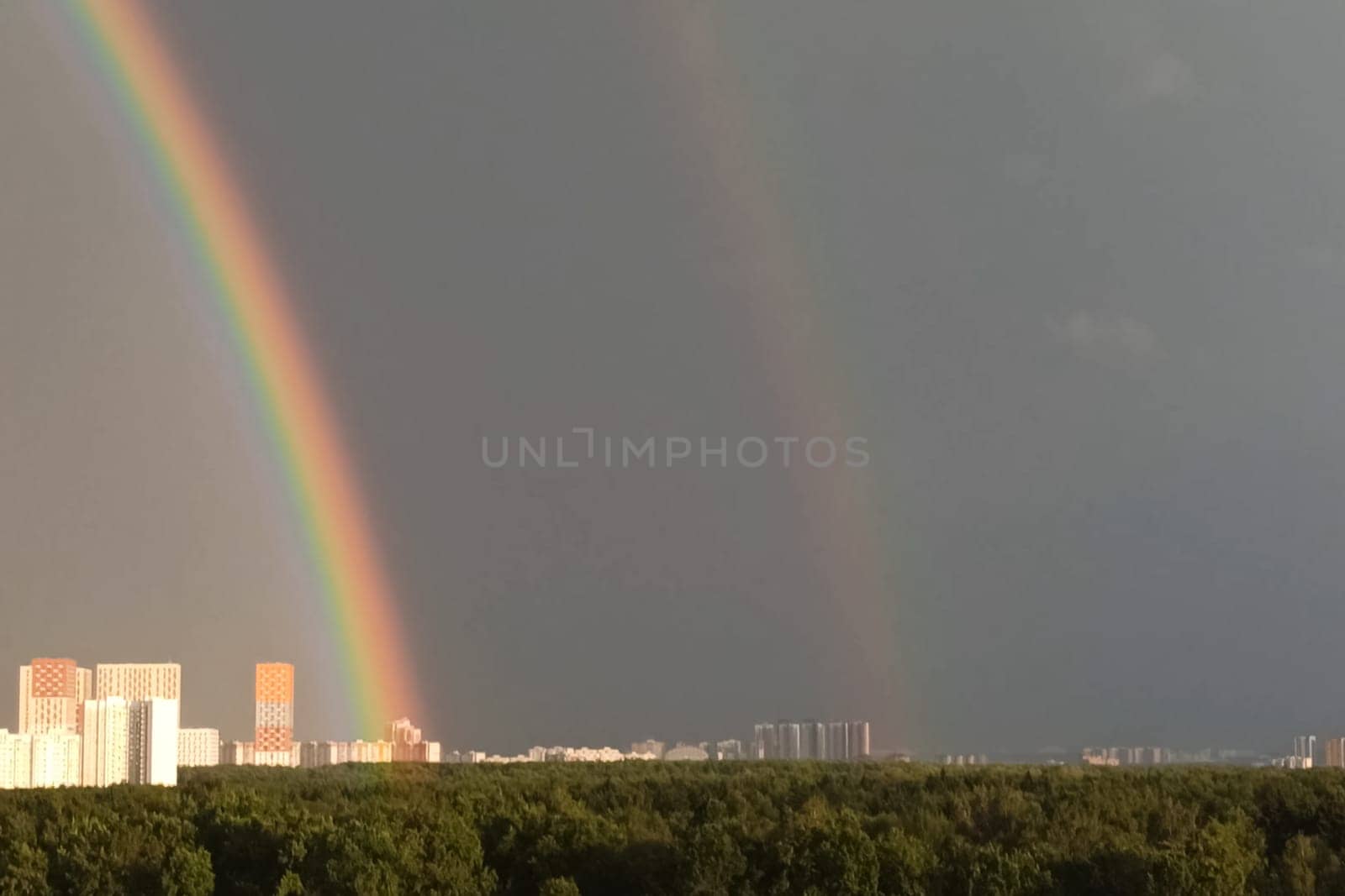 Tower cranes against the sky with clouds and rainbow.
