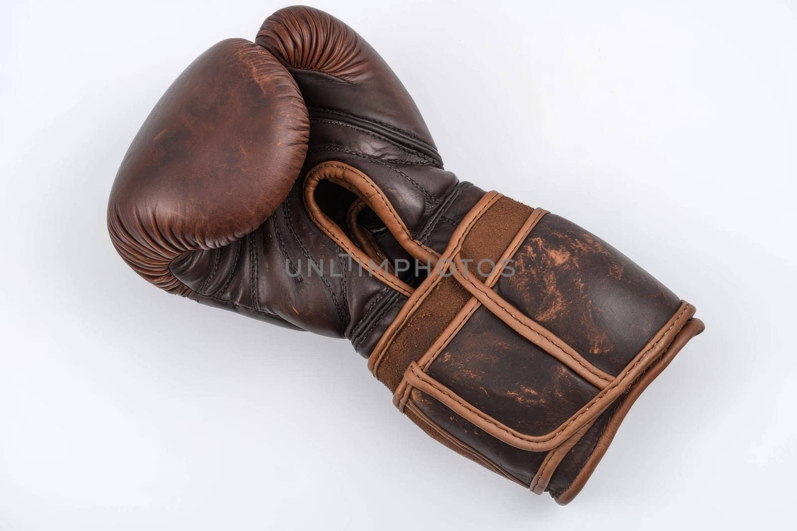 A well-worn, brown boxing glove lies flat against a neutral backdrop, showcasing its unique character and history in sports.