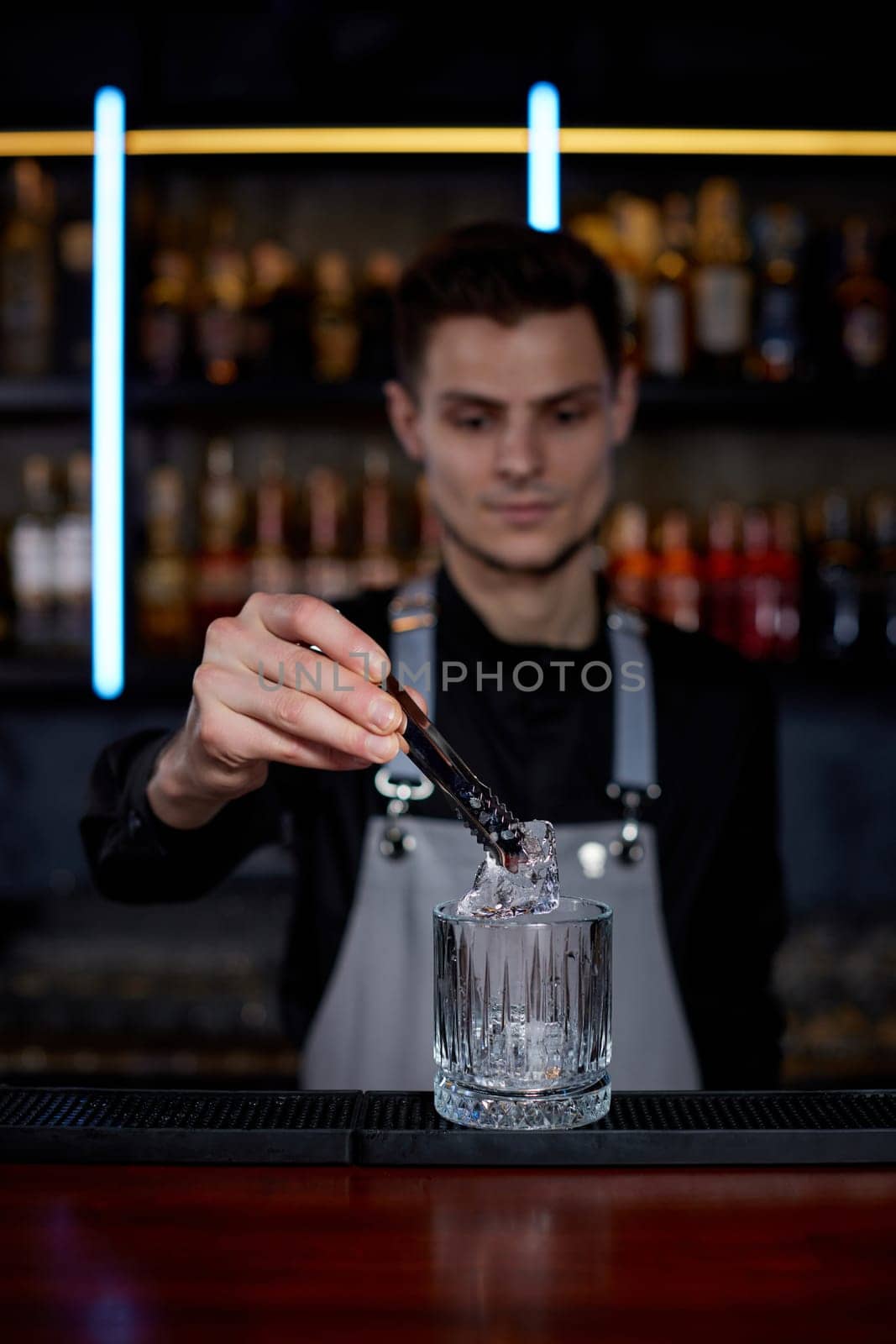 Barman puts the ice cubes into a glass with alcoholic drink at the bar
