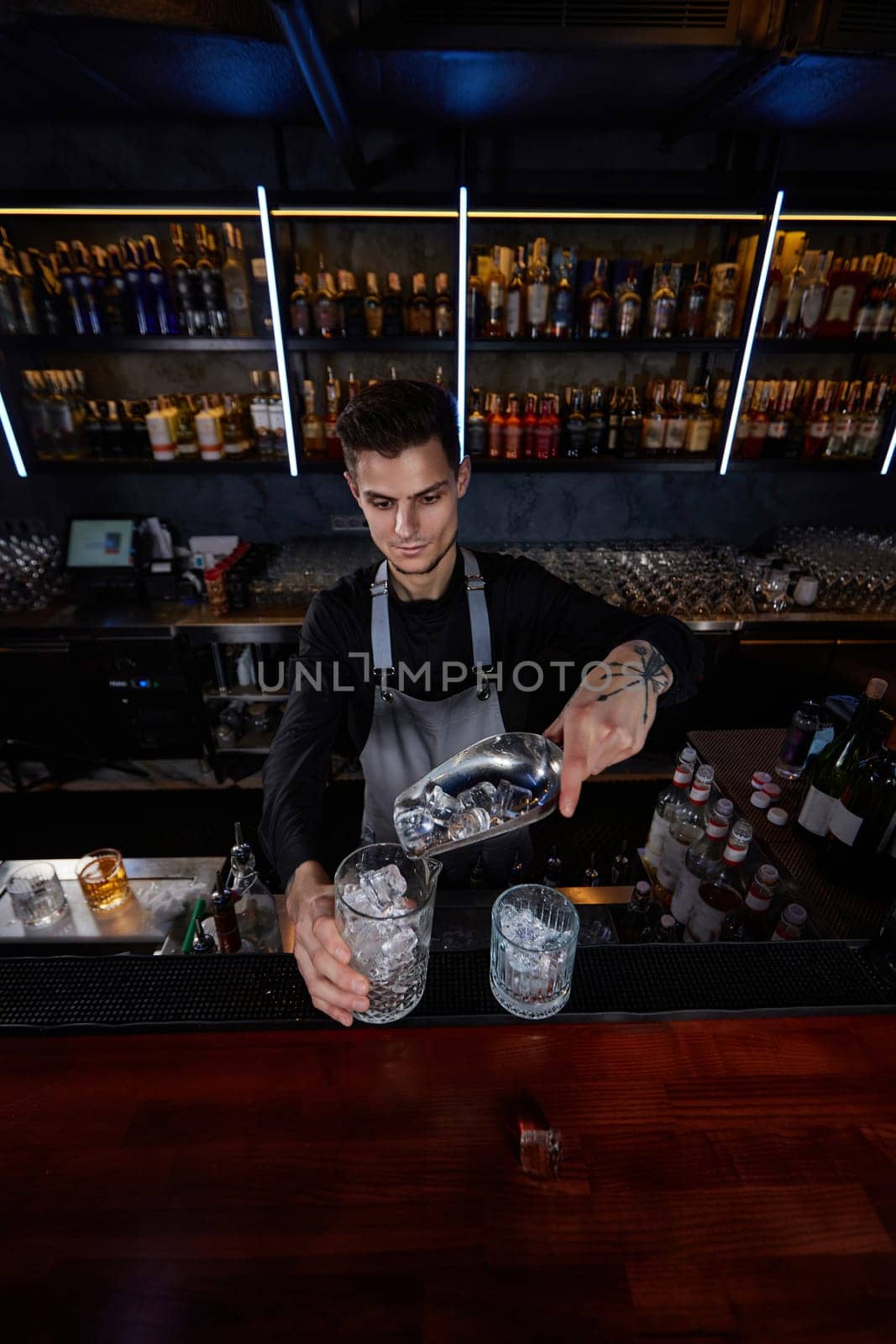 Barman puts the ice cubes into a glass with alcoholic drink at the bar