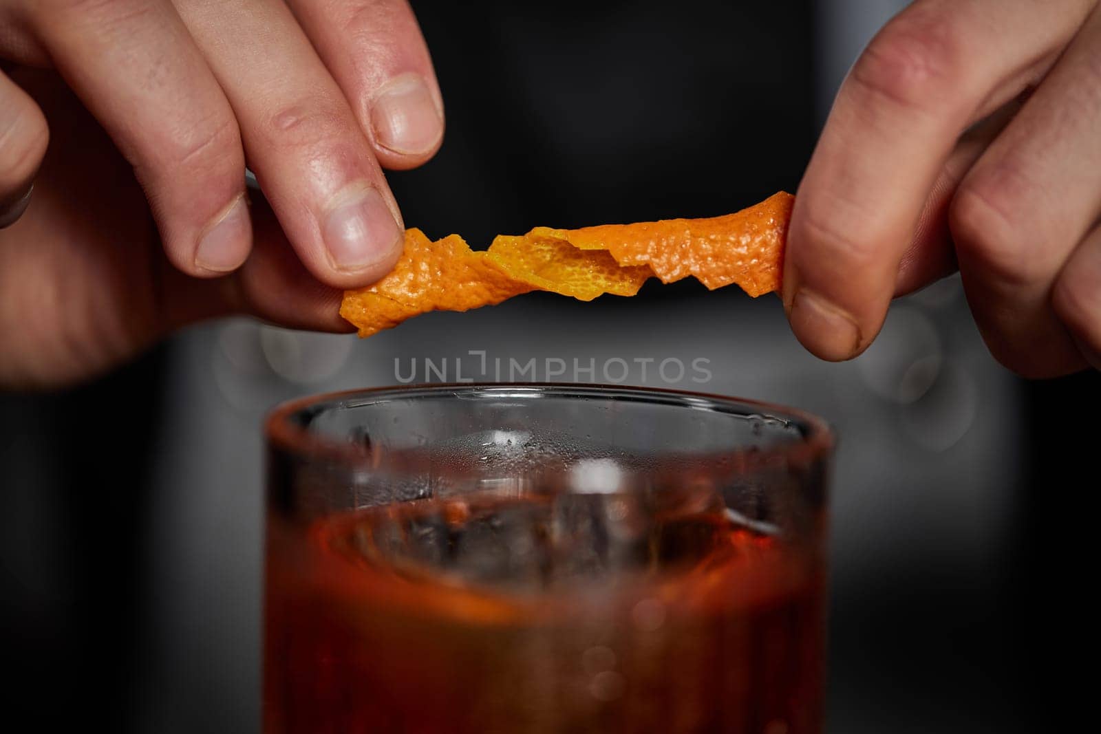 bartender makes a cocktail in a glass with orange peel at the bar, close-up