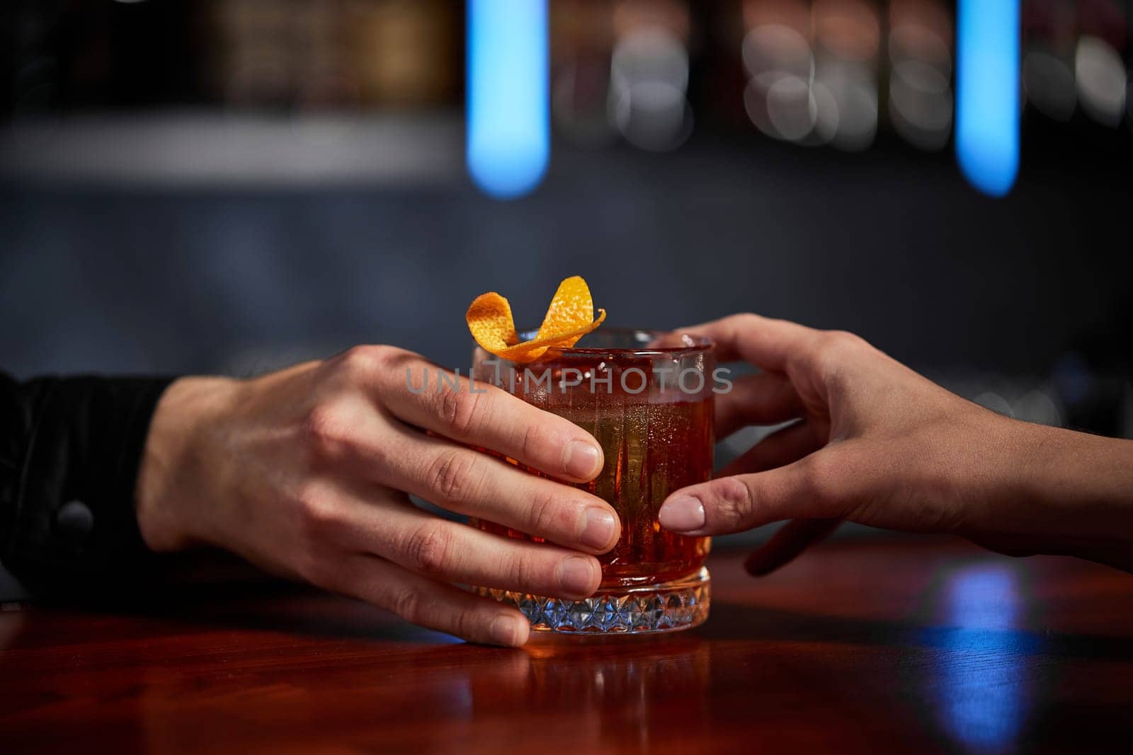 Barman holding out glass with alcoholic cocktail to the client. close-up