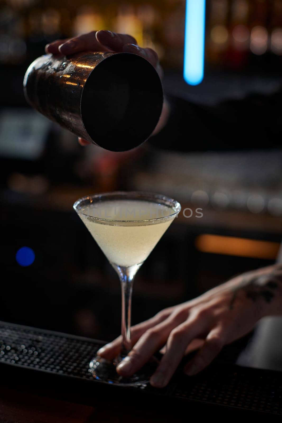 male barman hands is making cocktail with steel shaker at the bar counter, close-up