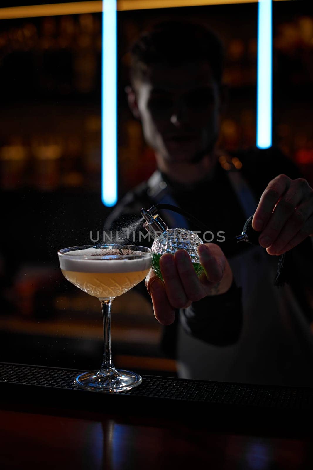 barman splashing absinthe from siphon on glass of cocktail