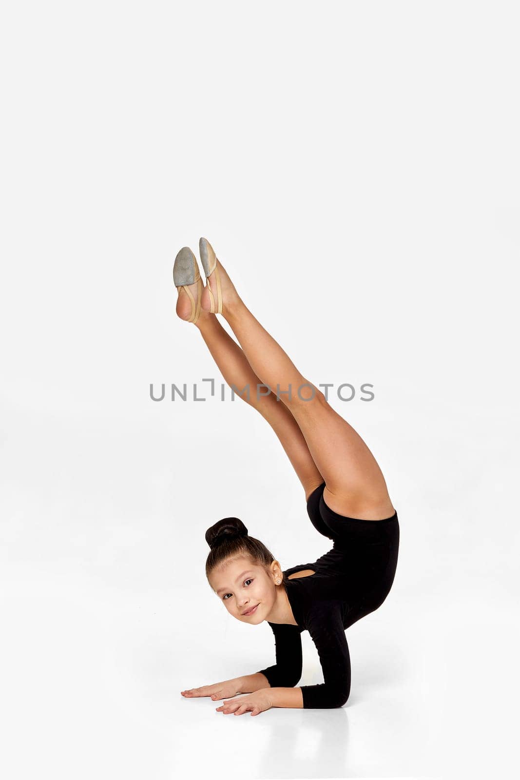 adorable little gymnast child girl in black sportswear performs a handstand.