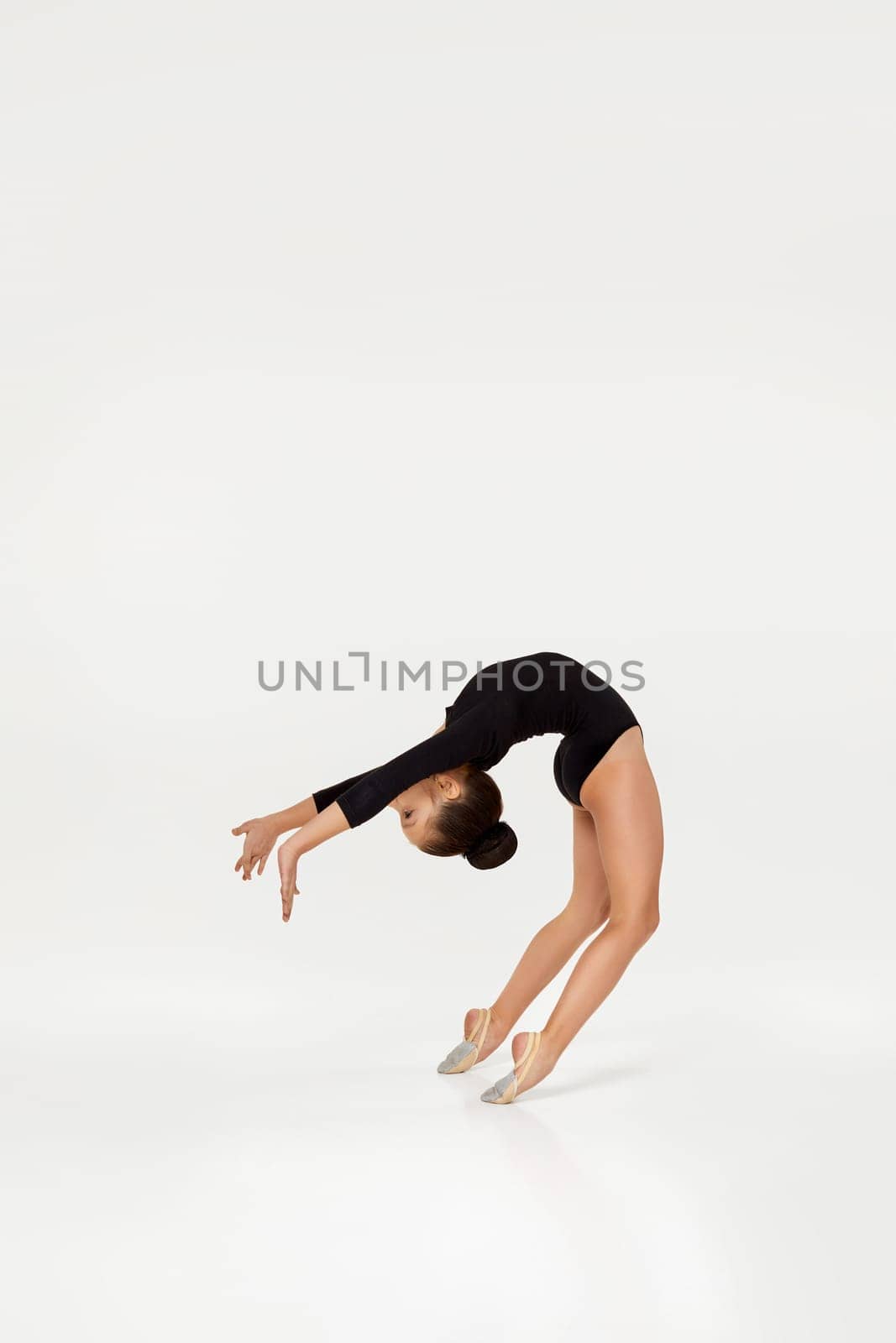 modern style dancer on studio background. little gymnast girl in black sportswear performs gymnastic poses.