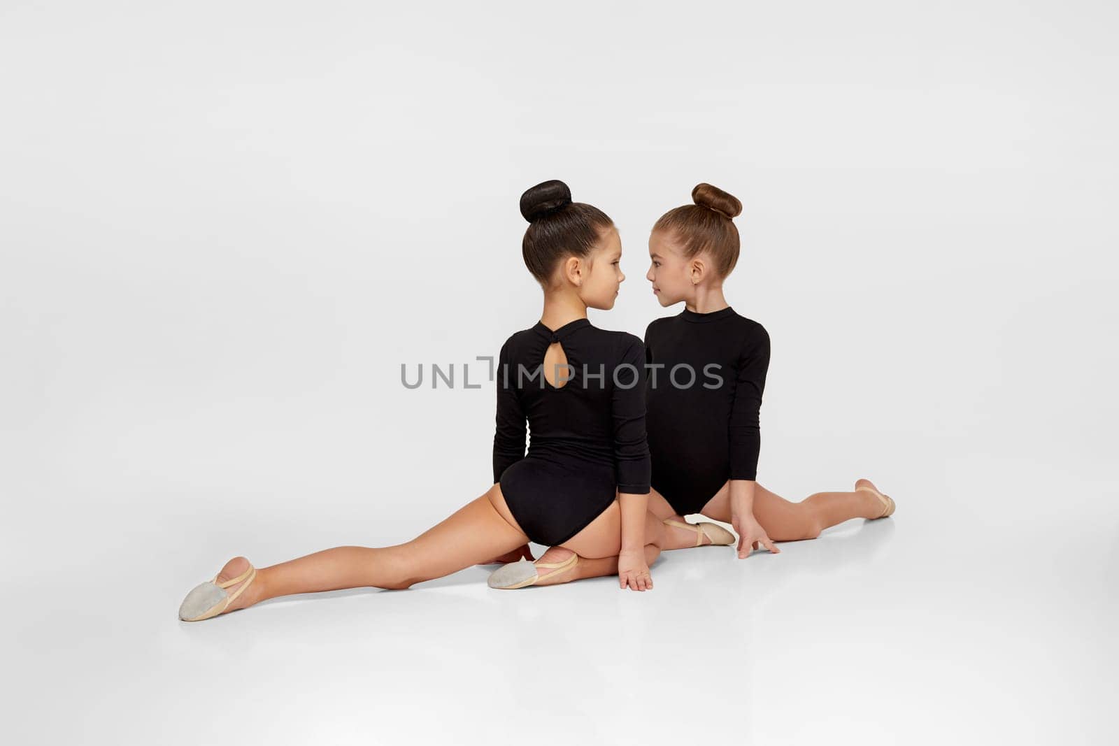 two young beautiful gymnast girls in black sportswear performs gymnastic poses