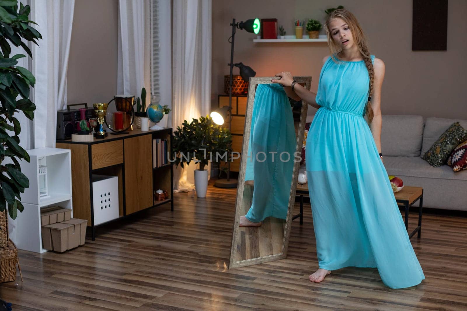 A woman showcases a vibrant blue dress in a chic living room setting, blending fashion with interior design.
