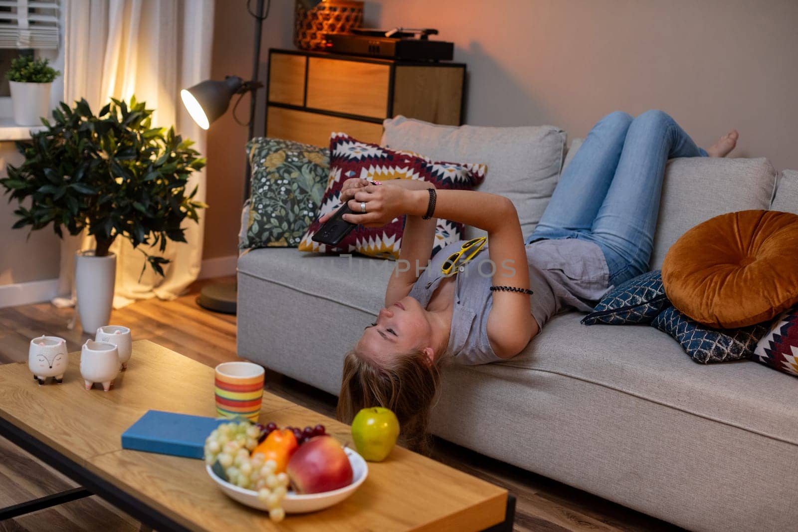 A cozy scene of a person relaxing on a couch, enjoying snacks and engaging with mobile entertainment