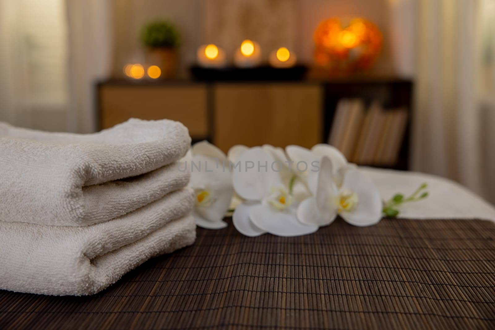 A serene and peaceful spa setting that showcases soft fluffy towels, tranquil flowers, and warm candlelight ambiance
