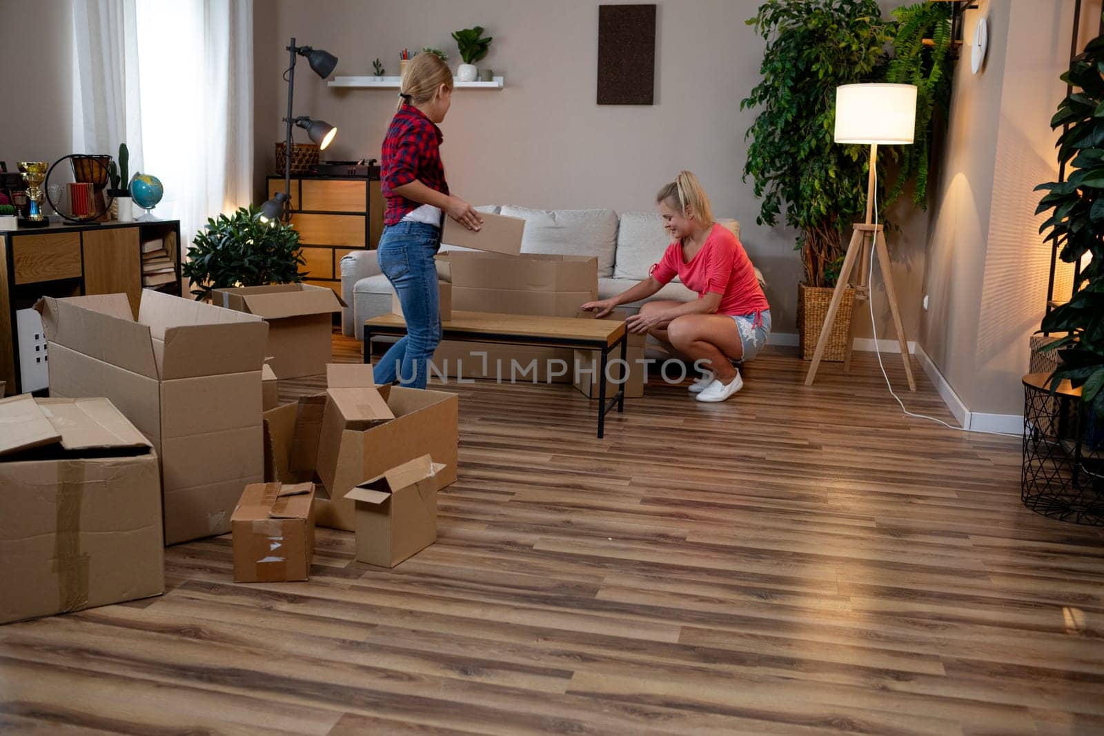 Two friends are happily unpacking boxes and carefully organizing furniture in a cozy living room space together