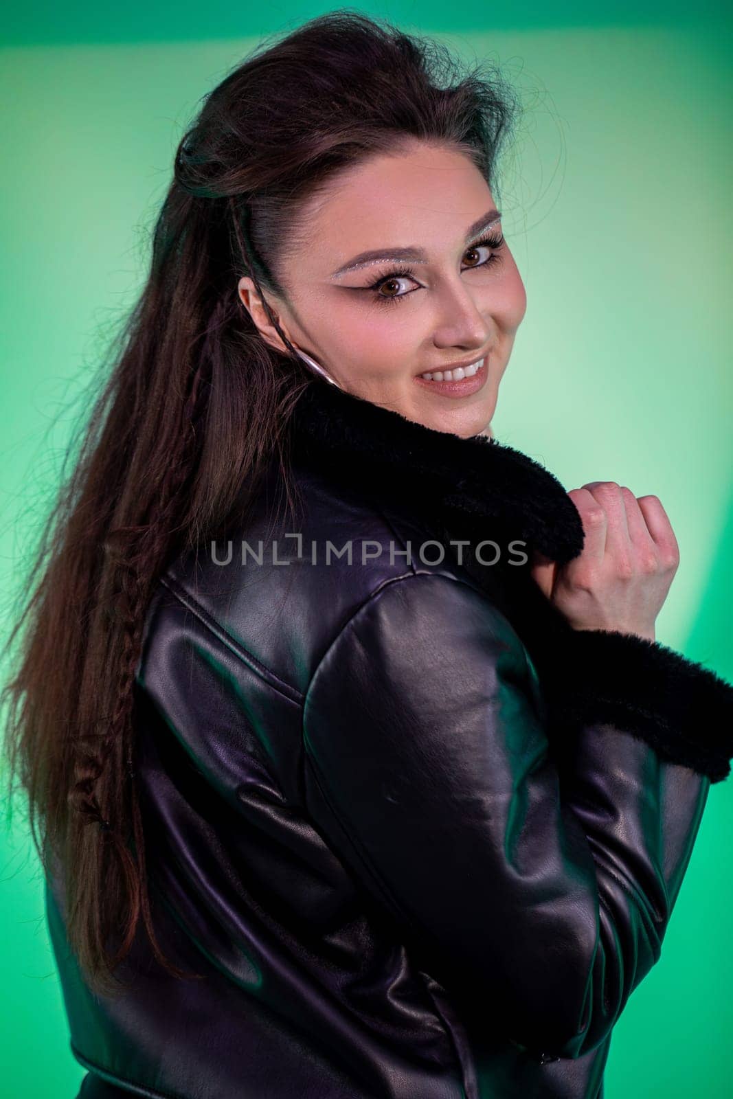 A young woman with long hair poses confidently in a leather jacket against an eyecatching vibrant backdrop