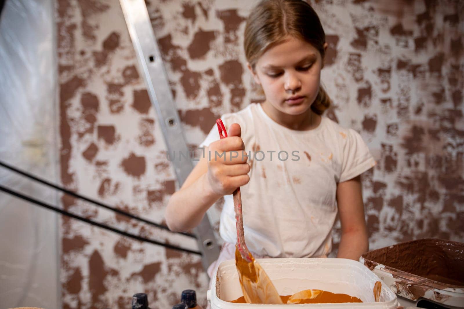 A young girl is deeply focused on her painting in a rustic and creatively inspiring environment around her