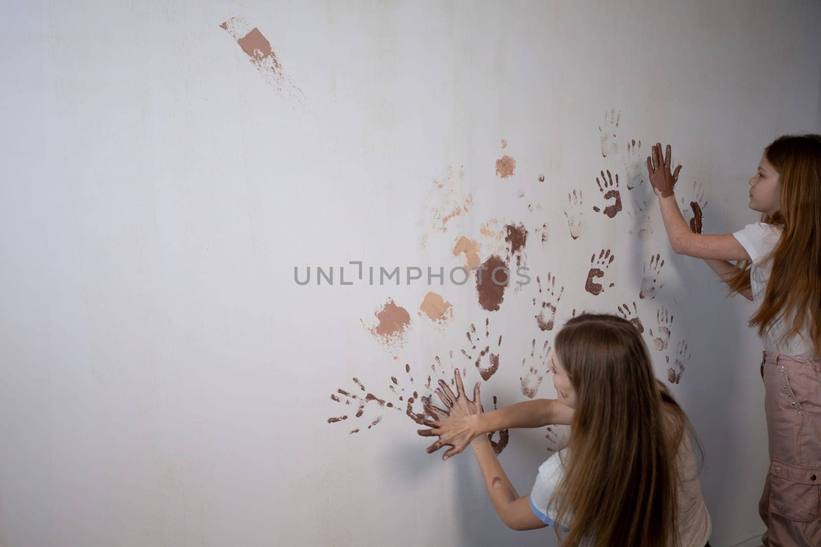 In a modern setting, children joyfully engage in playful creativity as they paint a wall with their hands