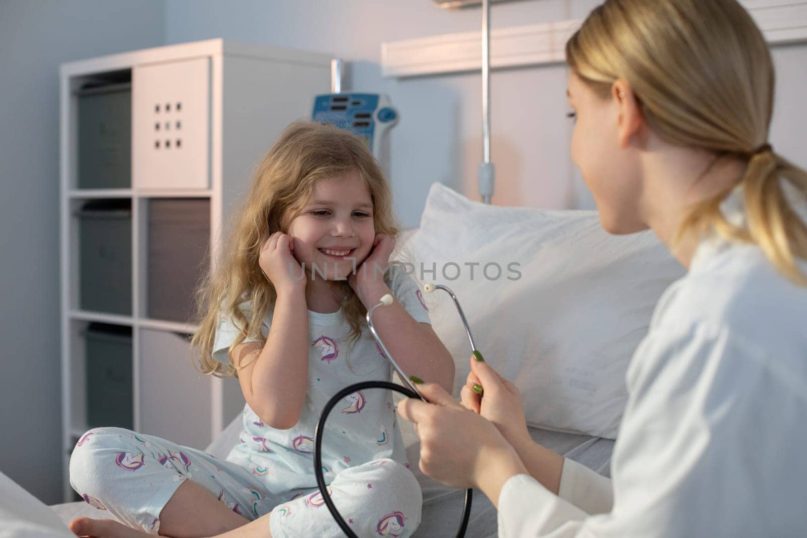 In a hospital setting, a young girl beams with joy while a caring nurse attentively listens using a stethoscope