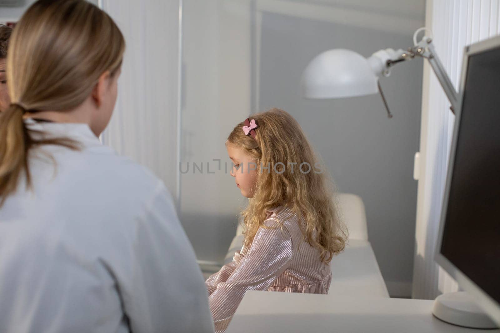In a bright and contemporary workspace, a young girl is sitting at a desk while an adult is nearby, supporting her