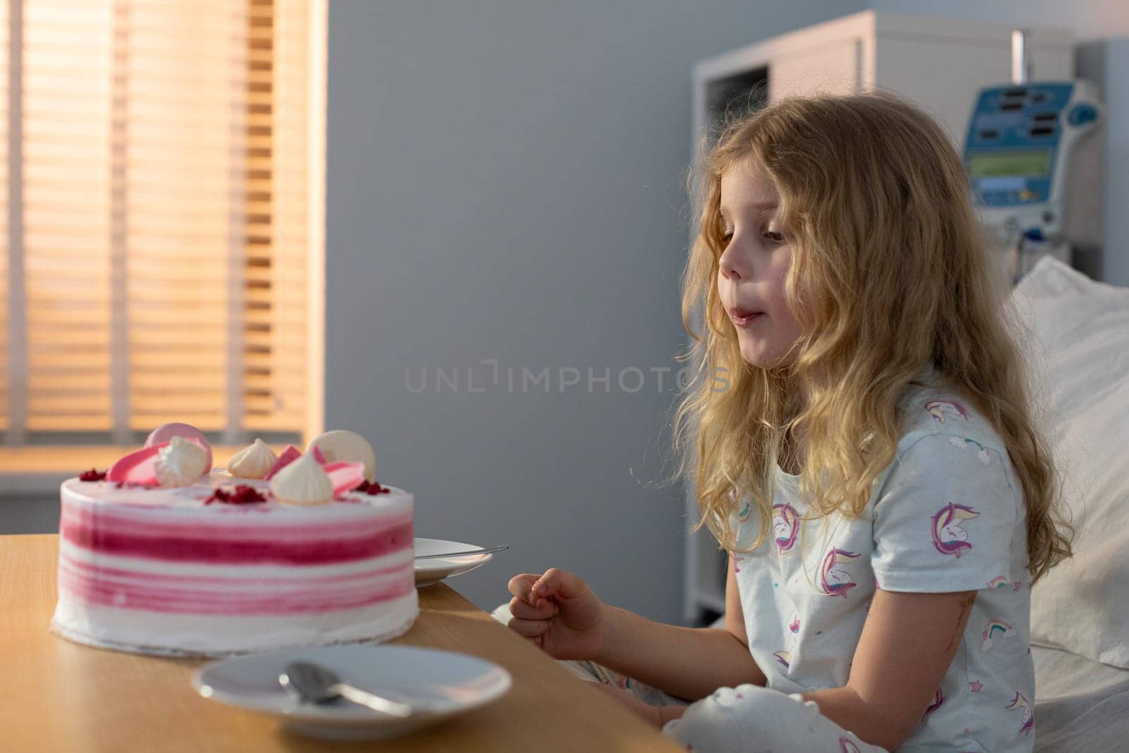 A young girl happily enjoys her birthday cake in a hospital setting, radiating pure joy and warmth to everyone around