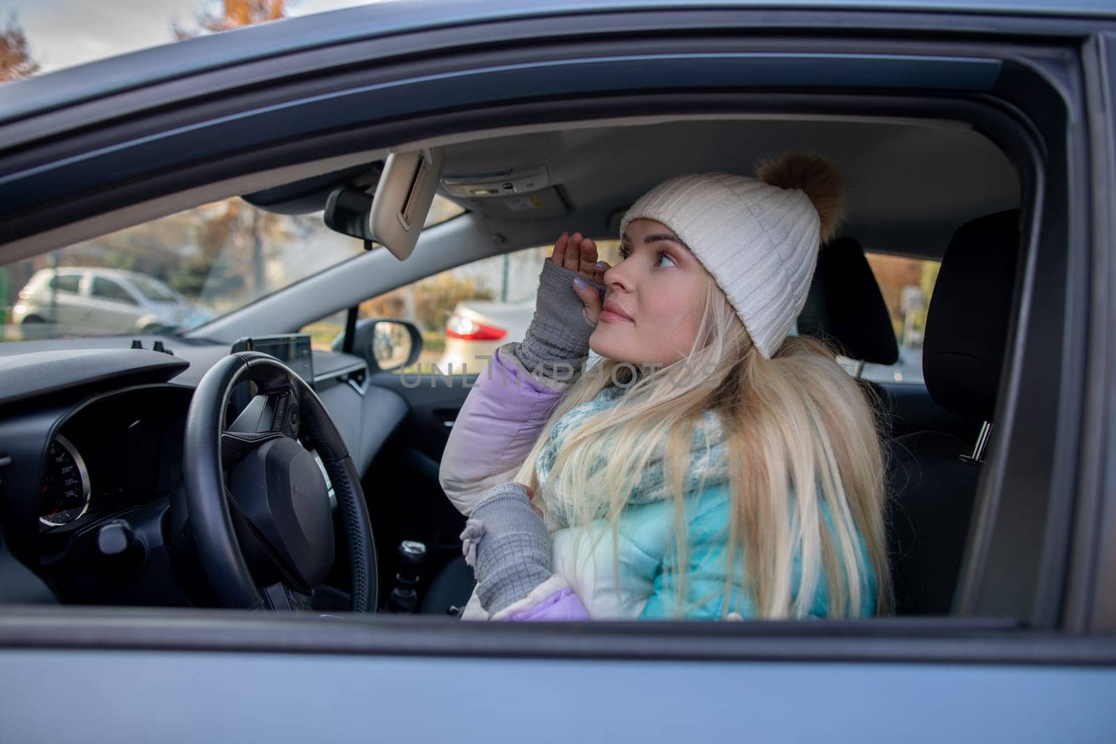 A woman dressed in a warm and cozy winter outfit is seen reflecting in her car on a chilly winter day