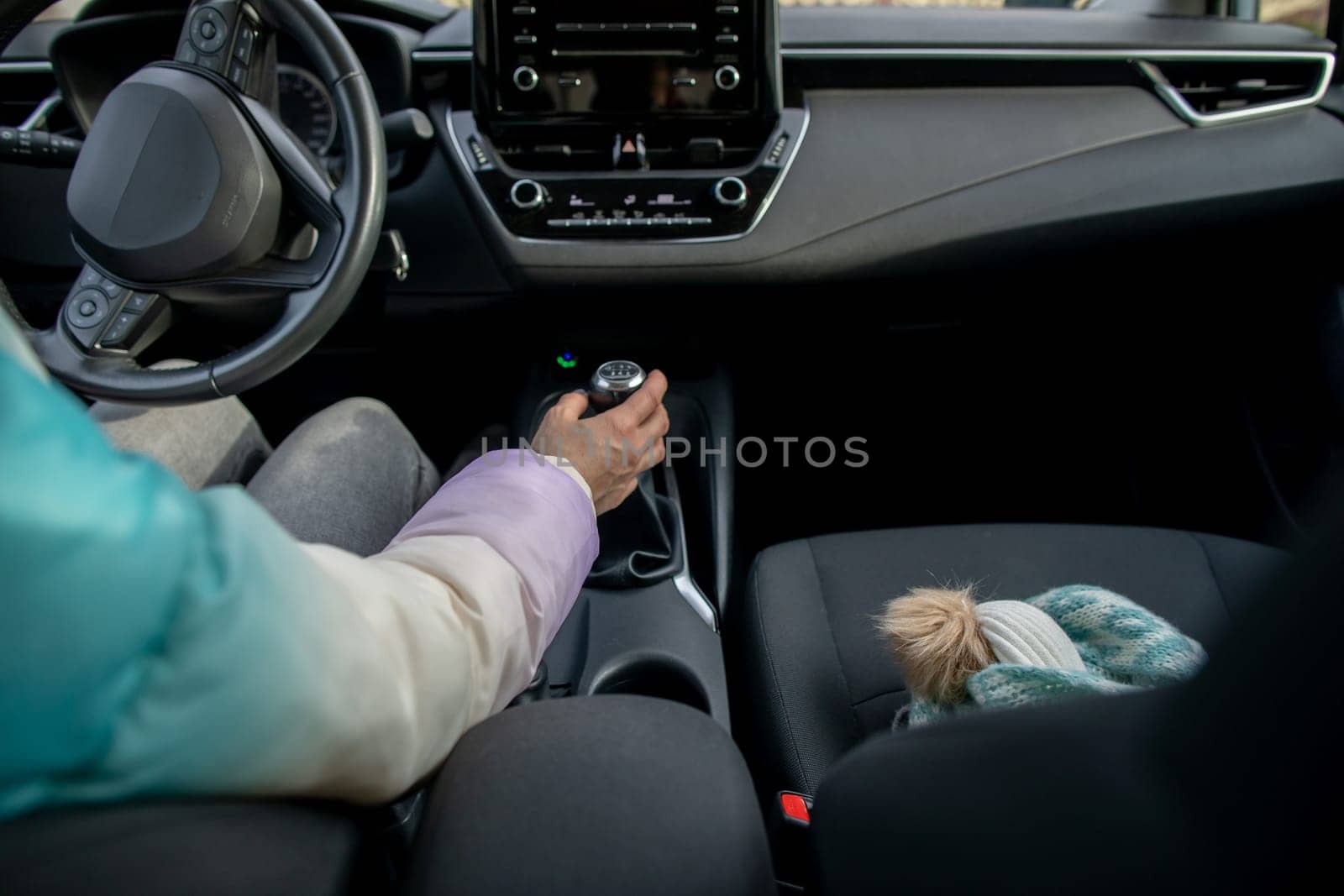 A beautifully designed car interior showcases a drivers hand poised on the gear shifter with a cute soft toy nearby
