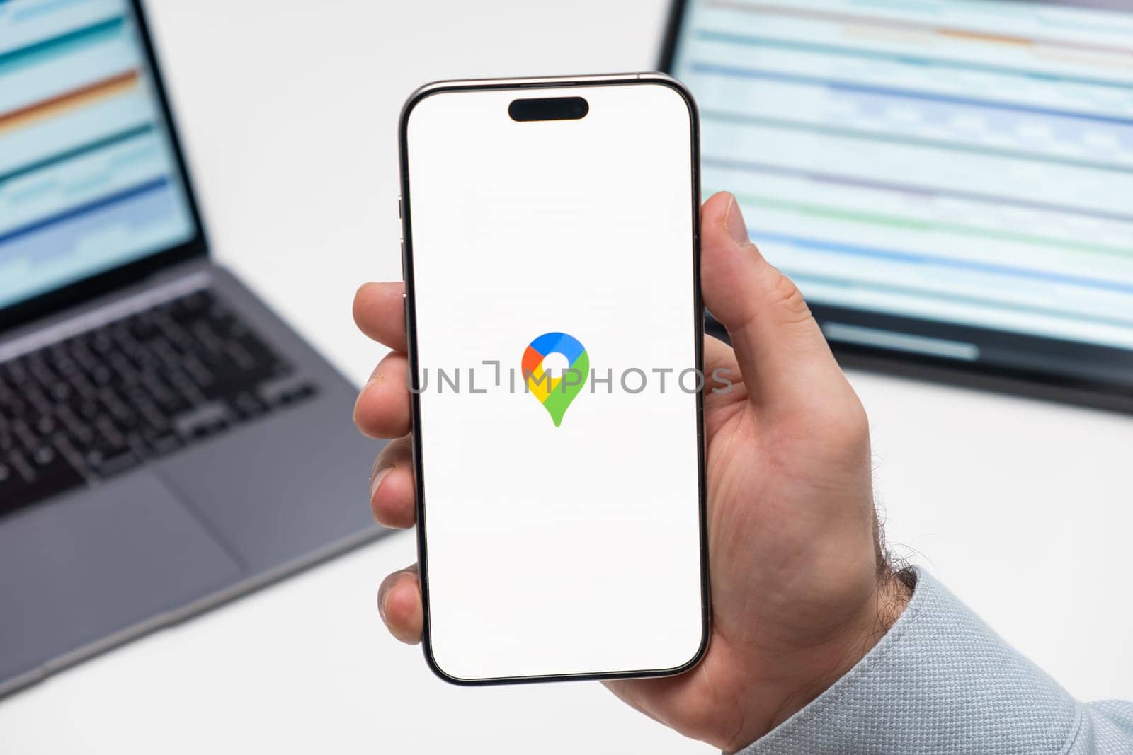 PRAGUE, CZECHIA - JULY, 2024: Google Maps logo on the screen of smartphone in mans hand and laptop on the background