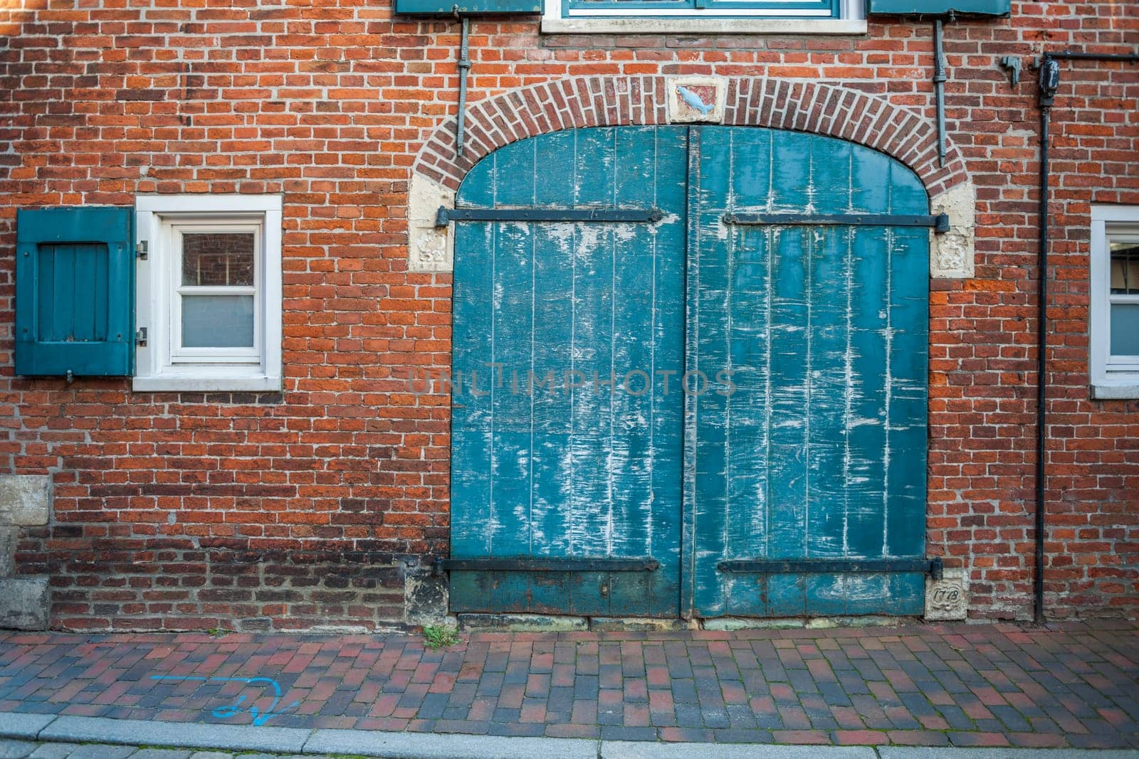 Frontal view of an old brick facade with a closed gate and small windows on both sides.