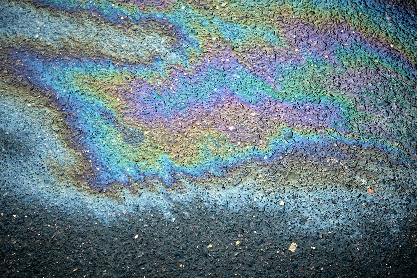 Gasoline rainbow creating colorful pattern on asphalt road
