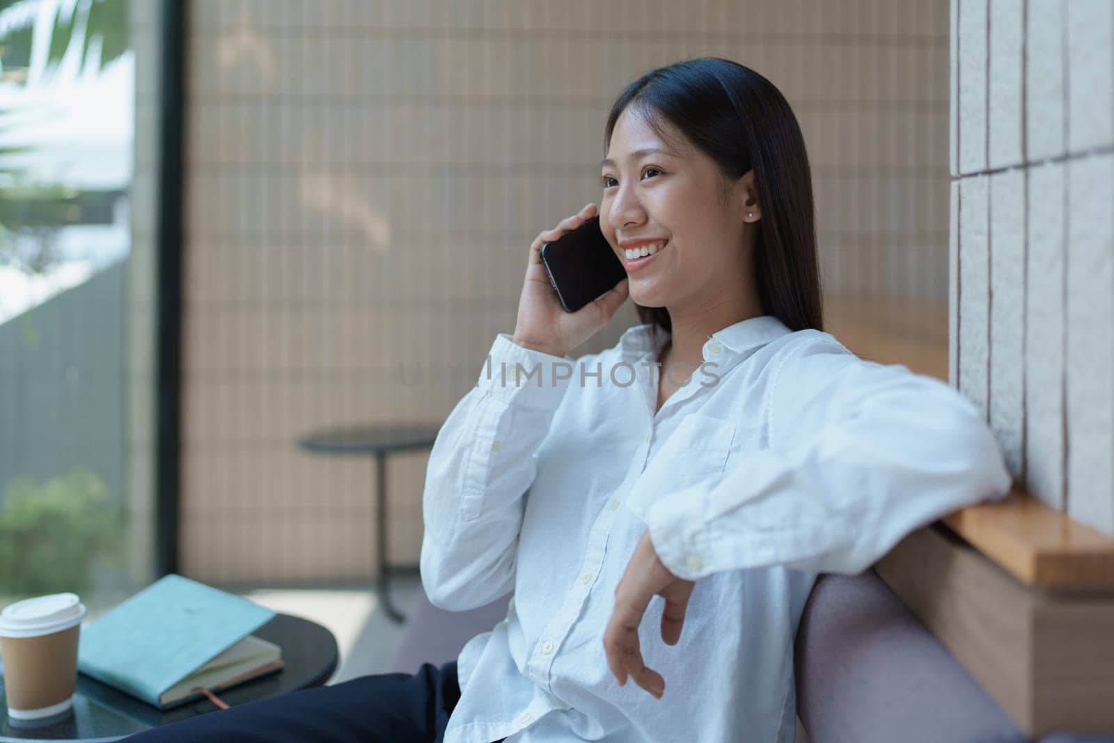 Happy young woman engaged in a phone conversation while relaxing in a bright modern cafe setting.