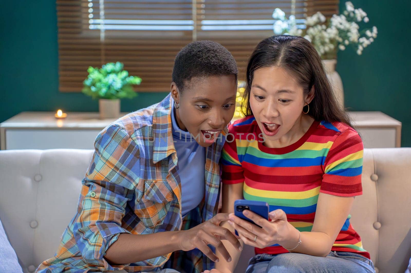 Two friends are sharing an exciting and joyful moment while they both look at their phone together on the couch