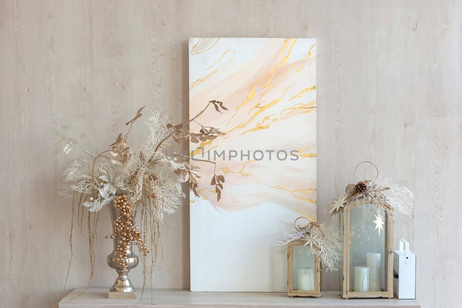 an abstract canvas, a vase with Christmas decor and decorative lanterns with candles stand on a table against the wall. Close up
