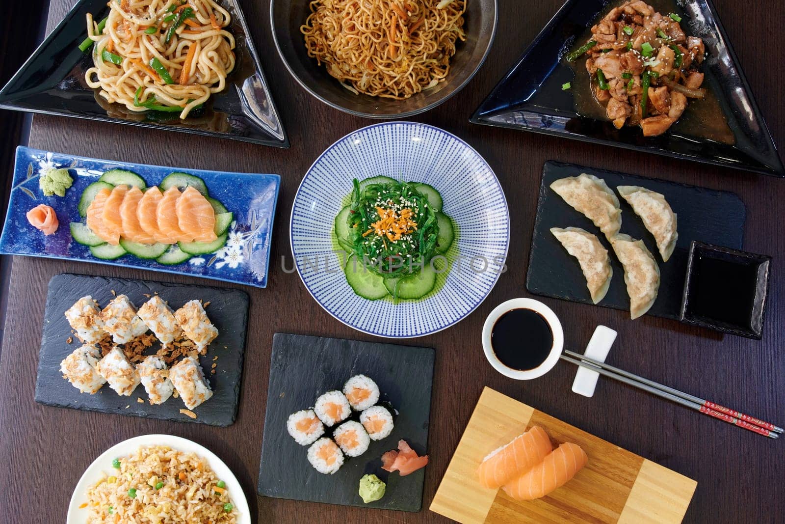A table full of Asian food including sushi, dumplings, and noodles. Scene is inviting and delicious